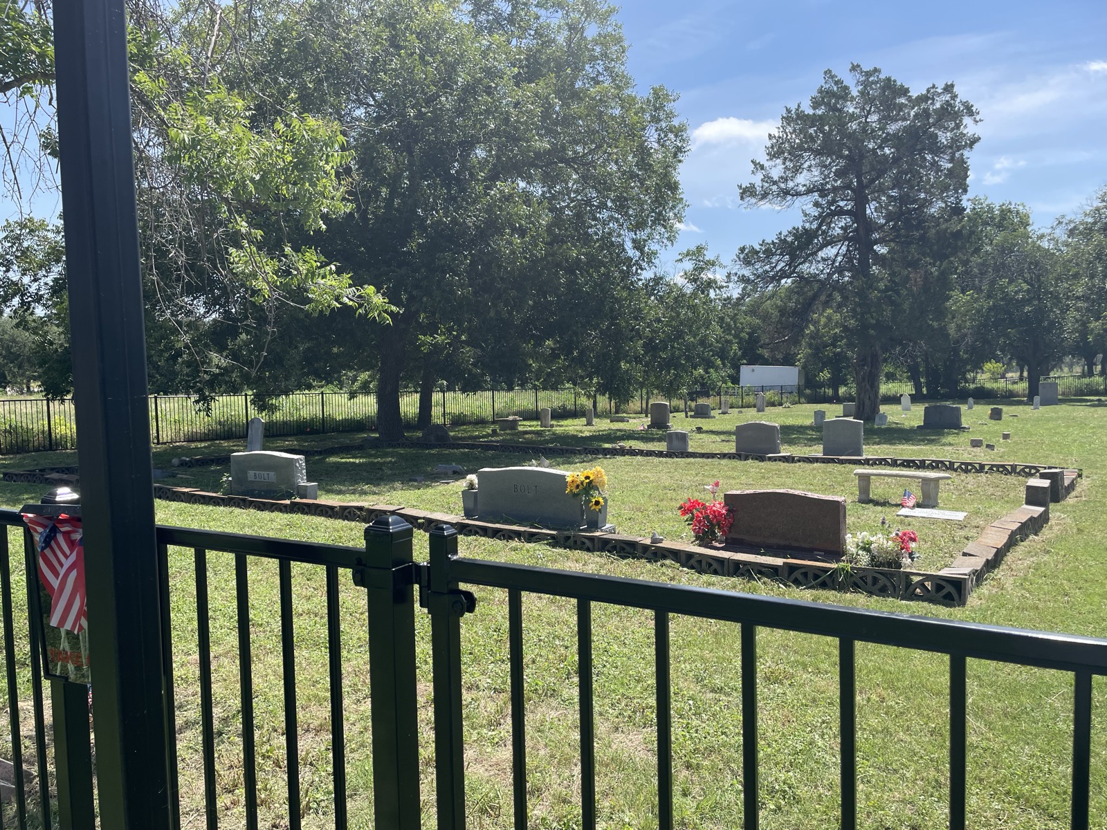 Neatly mowed grounds around curbed family plots with flowers, headstones and trees in the background.